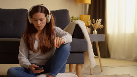 Mujer-Con-Auriculares-Inalámbricos-Sentada-En-El-Suelo-En-Casa-Transmitiendo-Música-Desde-Un-Teléfono-Móvil-13